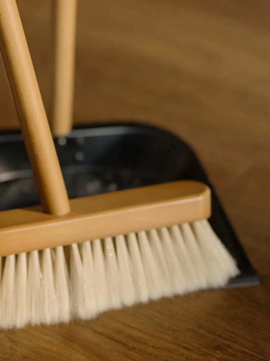 Broom and dustpan resting mid sweep on a warm wooden floor