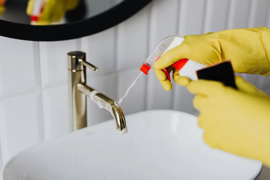Gloved hand detailing a brass faucet during a deep clean